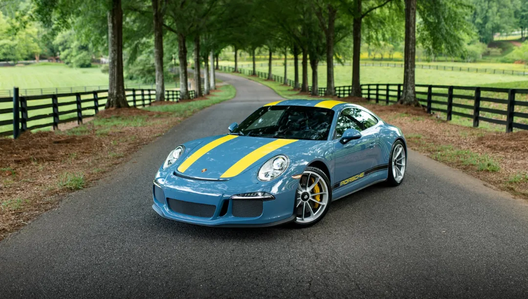 Blue Porsche 911 R with yellow stripes on a tree-lined driveway